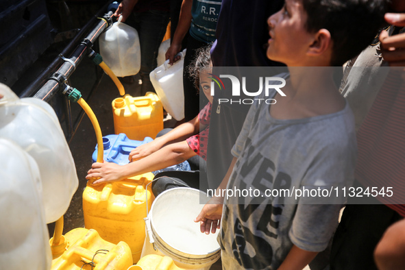 Palestinians are lining up to fill their containers with water on a street next to tents in Deir el-Balah, in the central Gaza Strip, on Jun...