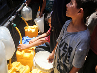 Palestinians are lining up to fill their containers with water on a street next to tents in Deir el-Balah, in the central Gaza Strip, on Jun...