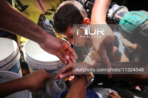 Palestinians are lining up to fill their containers with water on a street next to tents in Deir el-Balah, in the central Gaza Strip, on Jun...