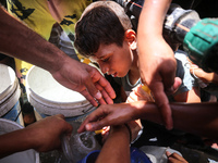 Palestinians are lining up to fill their containers with water on a street next to tents in Deir el-Balah, in the central Gaza Strip, on Jun...