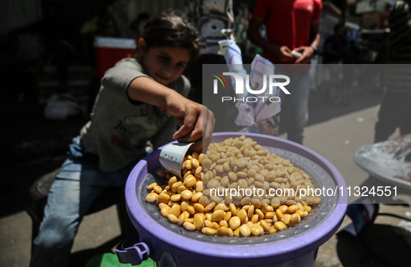 A displaced girl is selling lupin beans and waiting for customers on a street next to Al-Aqsa Martyrs Hospital in Deir el-Balah, in the cent...