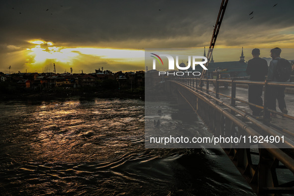 People are walking on a bridge during sunset after light rainfall in Sopore, Jammu and Kashmir, India, on June 12, 2024 