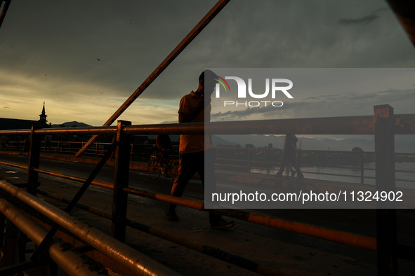 People are walking on a bridge during sunset after light rainfall in Sopore, Jammu and Kashmir, India, on June 12, 2024 