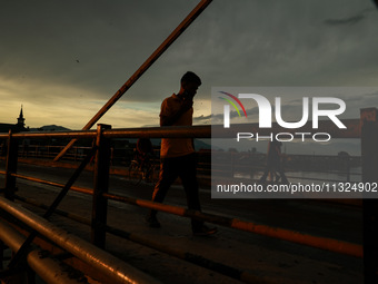 People are walking on a bridge during sunset after light rainfall in Sopore, Jammu and Kashmir, India, on June 12, 2024 (