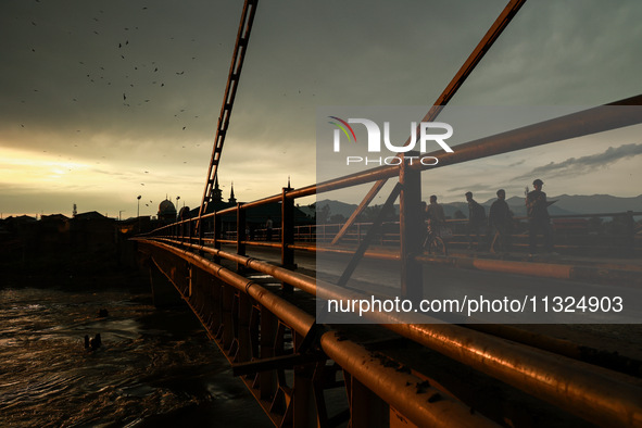 People are walking on a bridge during sunset after light rainfall in Sopore, Jammu and Kashmir, India, on June 12, 2024 