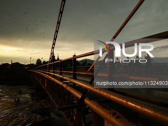 People are walking on a bridge during sunset after light rainfall in Sopore, Jammu and Kashmir, India, on June 12, 2024 (