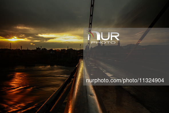 People are walking on a bridge during sunset after light rainfall in Sopore, Jammu and Kashmir, India, on June 12, 2024 