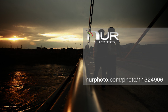 People are walking on a bridge during sunset after light rainfall in Sopore, Jammu and Kashmir, India, on June 12, 2024 