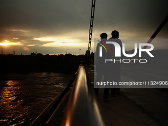 People are walking on a bridge during sunset after light rainfall in Sopore, Jammu and Kashmir, India, on June 12, 2024 (