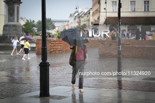 A man with an umbrella is seen walking barefoot during a rain storm in Warsaw, Poland on 02 June, 2024. 