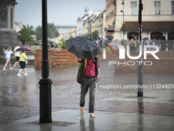 A man with an umbrella is seen walking barefoot during a rain storm in Warsaw, Poland on 02 June, 2024. (