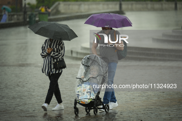 People with a child in a buggy are seen sheltering from a sudden downpour in Warsaw, Poland on 02 June, 2024. 