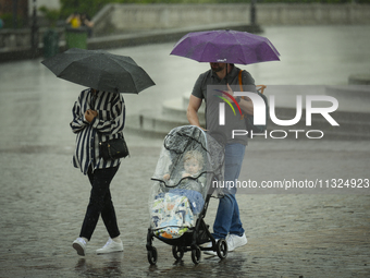 People with a child in a buggy are seen sheltering from a sudden downpour in Warsaw, Poland on 02 June, 2024. (