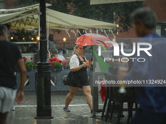 A waitress carrying coffee and rinks is seen during a sudden downpour in Warsaw, Poland on 02 June, 2024. (