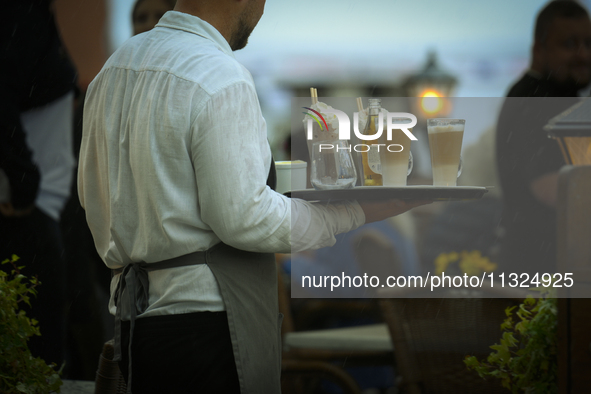 A waiter carrying coffee and rinks is seen during a sudden downpour in Warsaw, Poland on 02 June, 2024. 