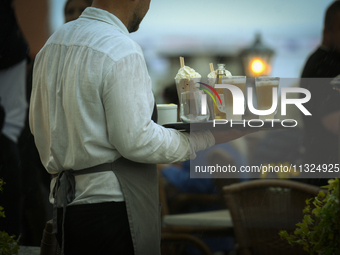 A waiter carrying coffee and rinks is seen during a sudden downpour in Warsaw, Poland on 02 June, 2024. (