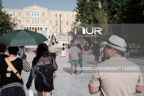 Tourists are wearing hats and holding umbrellas to protect from the sun at Syntagma Square during a heatwave in Athens, Greece, on June 12,...