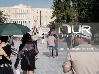 Tourists are wearing hats and holding umbrellas to protect from the sun at Syntagma Square during a heatwave in Athens, Greece, on June 12,...