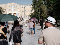 Tourists are wearing hats and holding umbrellas to protect from the sun at Syntagma Square during a heatwave in Athens, Greece, on June 12,...