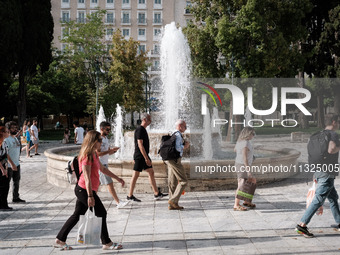 Tourists are walking in front of a fountain at Syntagma Square during a heatwave in Athens, Greece, on June 12, 2024. Many of the country's...