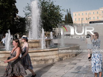 Tourists are walking in front of a fountain at Syntagma Square during a heatwave in Athens, Greece, on June 12, 2024. Many of the country's...