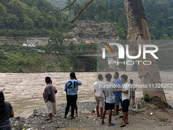 Residents are standing at the river banks of Teesta River to see the risen water level of the river, which flows beside National Highway 10,...