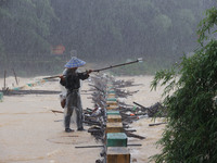 A villager is braving the rain to clear a tree branch stuck on a bridge in Dantan Township, Rongan County, Liuzhou, China, on June 13, 2024....