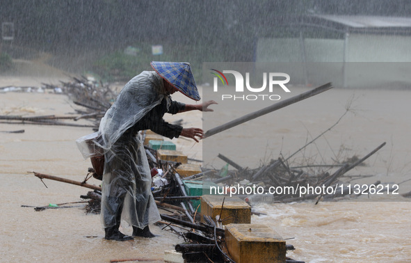 A villager is braving the rain to clear a tree branch stuck on a bridge in Dantan Township, Rongan County, Liuzhou, China, on June 13, 2024....