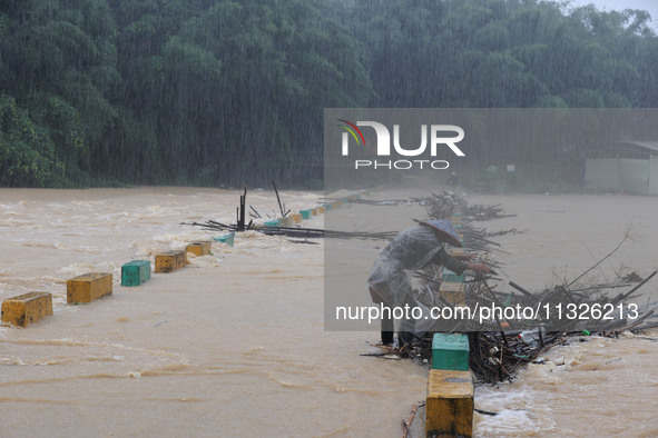 A villager is braving the rain to clear a tree branch stuck on a bridge in Dantan Township, Rongan County, Liuzhou, China, on June 13, 2024....