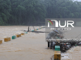 A villager is braving the rain to clear a tree branch stuck on a bridge in Dantan Township, Rongan County, Liuzhou, China, on June 13, 2024....