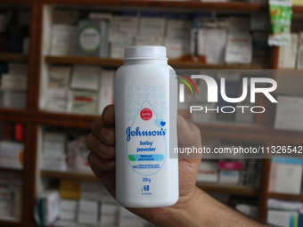 A man is holding a bottle of Johnson and Johnson Baby Powder at a drugstore in Srinagar, India, on June 13, 2024. Johnson & Johnson is agree...