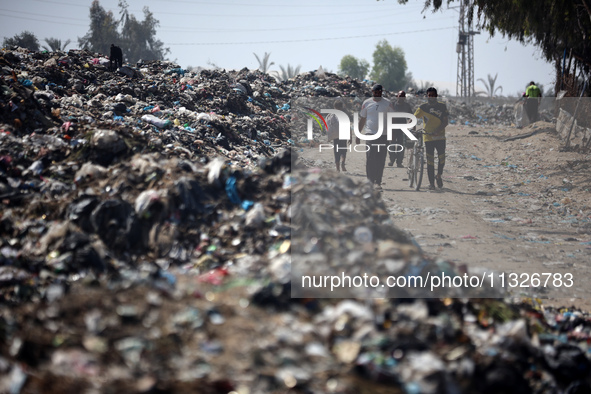 Palestinians are walking next to a garbage dump in Deir el-Balah, in the central Gaza Strip, on June 13, 2024, amid the ongoing conflict in...