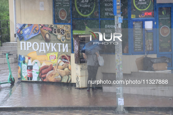 A woman is hiding under an umbrella during heavy rain, which is amounting to half of the monthly average, in Kyiv, Ukraine, on June 12, 2024...