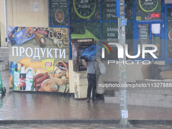 A woman is hiding under an umbrella during heavy rain, which is amounting to half of the monthly average, in Kyiv, Ukraine, on June 12, 2024...