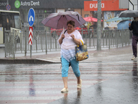 A woman is walking under an umbrella as she is crossing a street during heavy rain, which is amounting to half of the monthly average, in Ky...