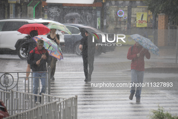 People are crossing a street with umbrellas during heavy rain, which is amounting to half of the monthly average, in Kyiv, Ukraine, on June...