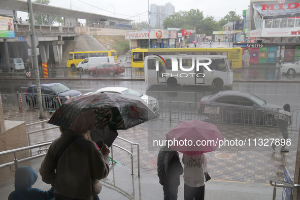 People with umbrellas are looking at public transport on the road during heavy rain, which is amounting to half of the monthly average, in K...