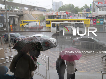 People with umbrellas are looking at public transport on the road during heavy rain, which is amounting to half of the monthly average, in K...