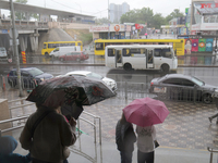 People with umbrellas are looking at public transport on the road during heavy rain, which is amounting to half of the monthly average, in K...