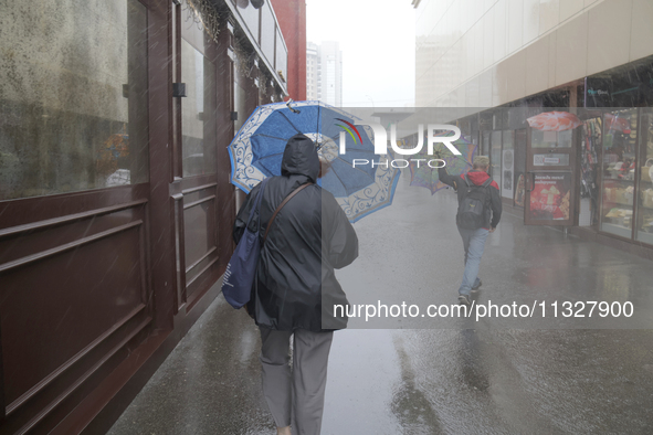 People are walking along a street with umbrellas during heavy rain, which is amounting to half of the monthly average, in Kyiv, Ukraine, on...