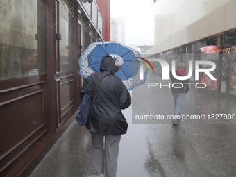 People are walking along a street with umbrellas during heavy rain, which is amounting to half of the monthly average, in Kyiv, Ukraine, on...