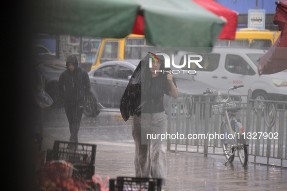 A woman is covering her head with a jacket during heavy rain, which has amounted to half of the monthly average, in Kyiv, Ukraine, on June 1...