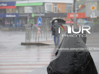 A woman is covering her head with a jacket during heavy rain, which has amounted to half of the monthly average, in Kyiv, Ukraine, on June 1...