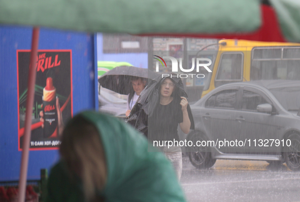 A woman is covering her head with a jacket during heavy rain, which has amounted to half of the monthly average, in Kyiv, Ukraine, on June 1...