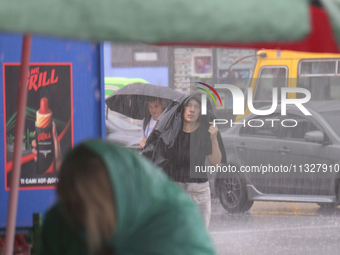 A woman is covering her head with a jacket during heavy rain, which has amounted to half of the monthly average, in Kyiv, Ukraine, on June 1...