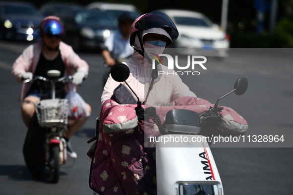 Citizens are wearing sun-protective clothing and riding on a street under high temperatures in Fuyang, China, on June 14, 2024. 