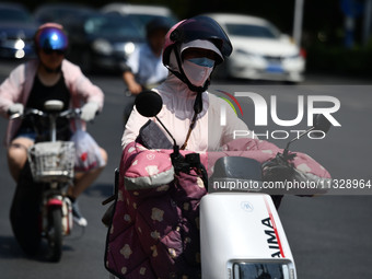 Citizens are wearing sun-protective clothing and riding on a street under high temperatures in Fuyang, China, on June 14, 2024. (