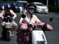 Citizens are wearing sun-protective clothing and riding on a street under high temperatures in Fuyang, China, on June 14, 2024. (