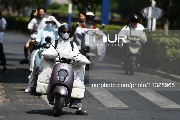 Citizens are wearing sun-protective clothing and riding on a street under high temperatures in Fuyang, China, on June 14, 2024. 