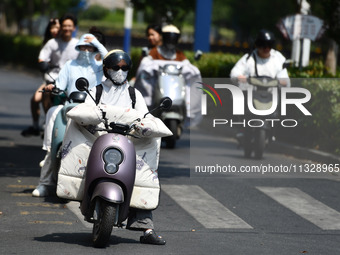 Citizens are wearing sun-protective clothing and riding on a street under high temperatures in Fuyang, China, on June 14, 2024. (